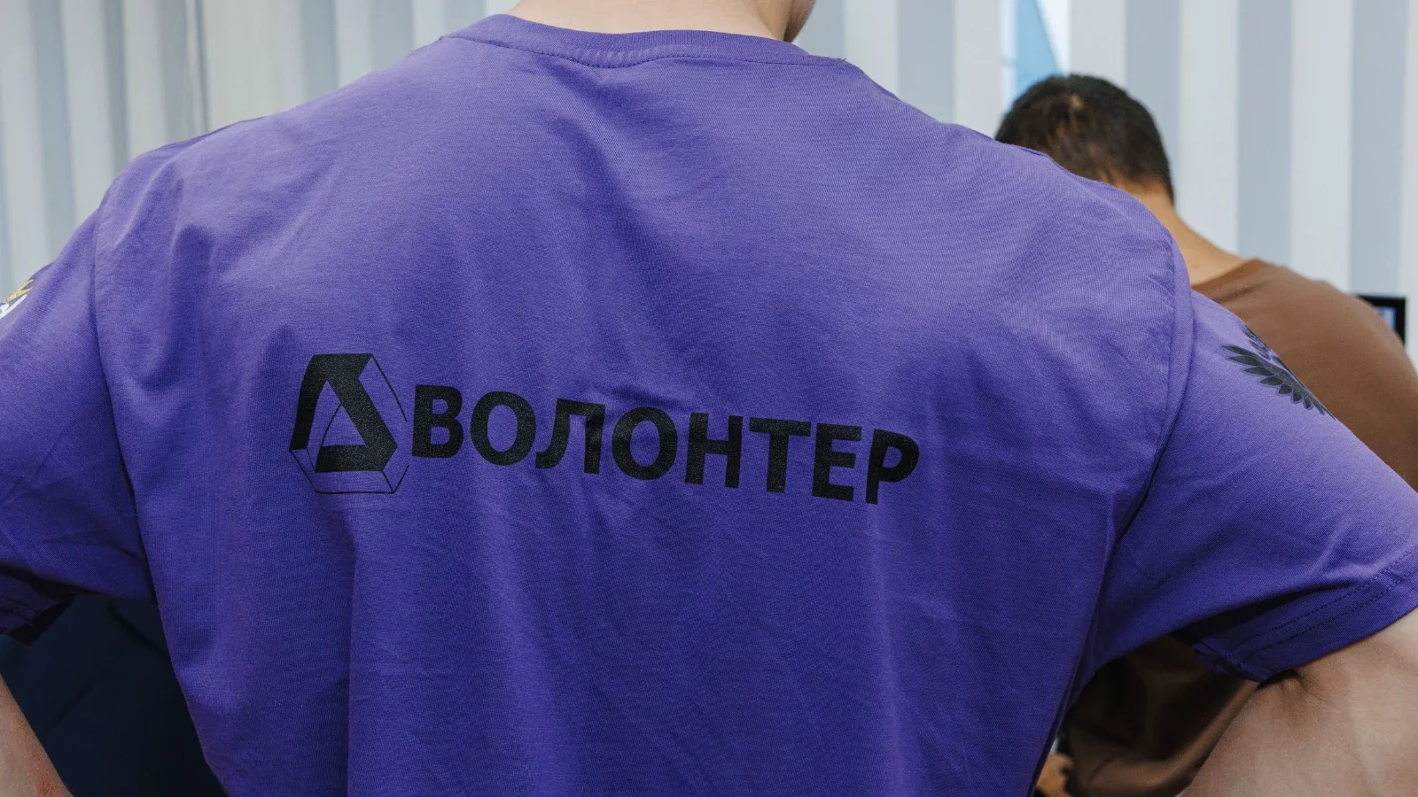 Человек в футболке с надписью «Волонтер»